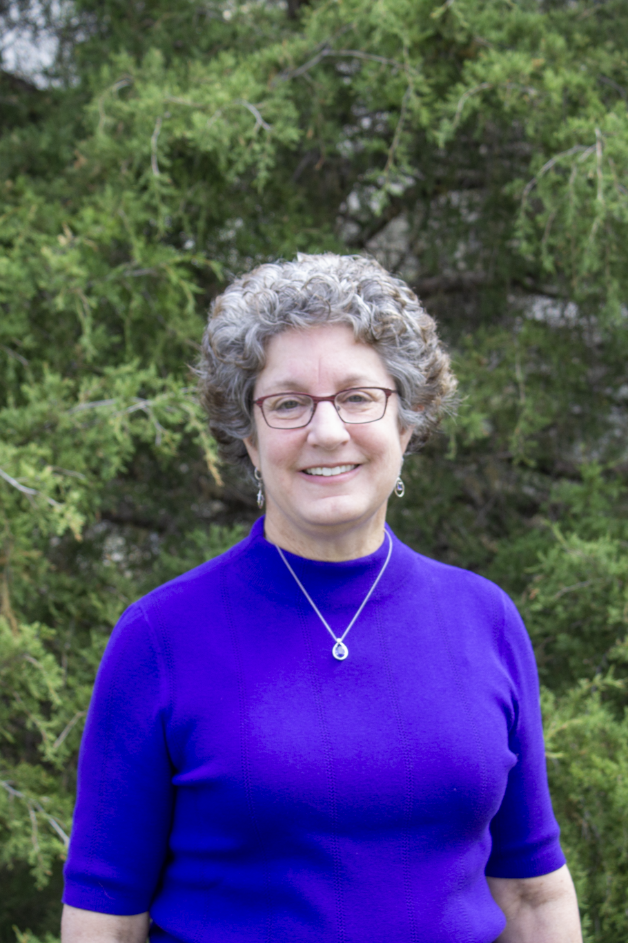 Headshot of Linda Caudill standing in front of bushes and Hokie Stone